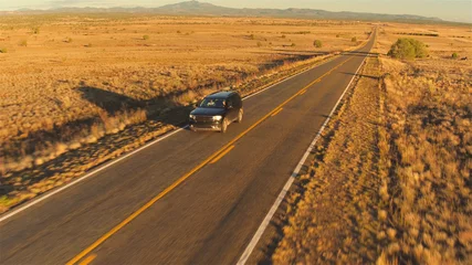 Poster AERIAL: SUV car driving along empty countryside road at sunset © helivideo