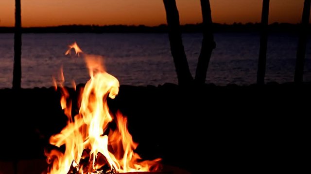 Beautiful lakeside campfire closeup just after sunset with trees along shoreline and ripples on lake