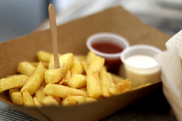 French fries with hot sauce and mayonnaise, served in a cardboard package. Common street food. Selective focus.