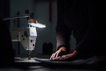 Sewing machine in dark with working hands on backdrop