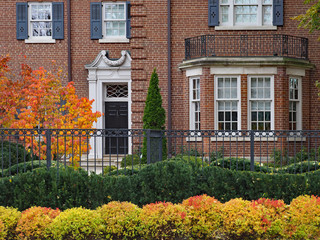 large brick house with iron fence and fall foliage