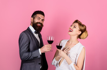Woman in dress and handsome man in suit dating in restaurant. Couple holds glass of red wine. Happy couple drinking red wine and flirting. Beautiful young couple with glasses of red wine in restaurant