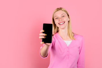 Fototapeta premium Smile girl hold mobile phone. Black Friday, cyber Monday. Advertising new model. Beautiful woman showing smart phone. Young beautiful woman holds smartphone with empty screen. Copy space for advertise
