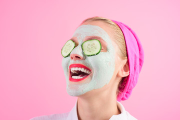 Beautiful young woman is getting facial clay mask at spa with cucumbers on eyes. Woman in cosmetic mask. Beauty, cosmetics, body care and spa concept. Spa woman caring for face skin and health.Closeup