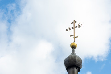 Orthodox cross close up on the tower of the middle church in the background of blue sky and clouds. The concept of Christianity, the symbol of the Orthodox faith in God