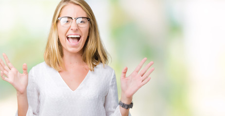 Beautiful young woman wearing glasses over isolated background crazy and mad shouting and yelling with aggressive expression and arms raised. Frustration concept.