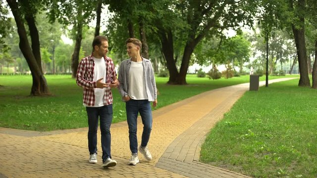 Father in his 40s walking with son in park, sharing his life experience and tips