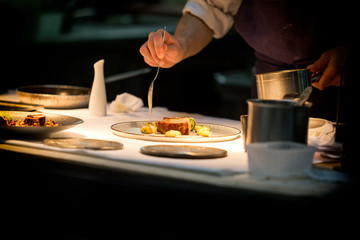 Chef preparing a plate made of meat and vegetables. The chef is pouring sauce on the plate. - obrazy, fototapety, plakaty