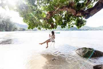 Beautiful young woman traveler swinging on a swing on a tropical island in the background of...