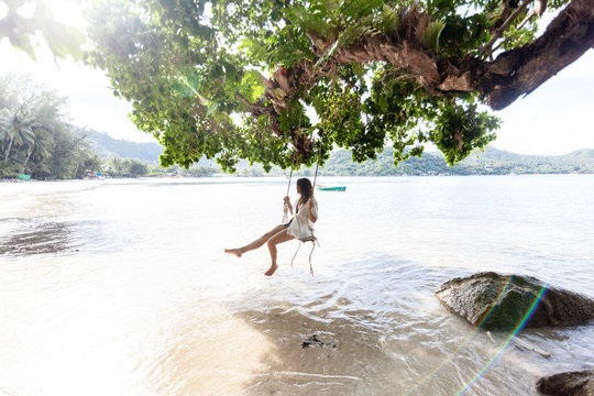 Beautiful young woman traveler swinging on a swing on a tropical island in the background of amazing landscape