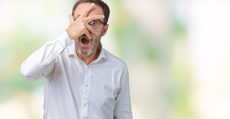 Handsome middle age elegant senior business man wearing glasses over isolated background peeking in shock covering face and eyes with hand, looking through fingers with embarrassed expression.