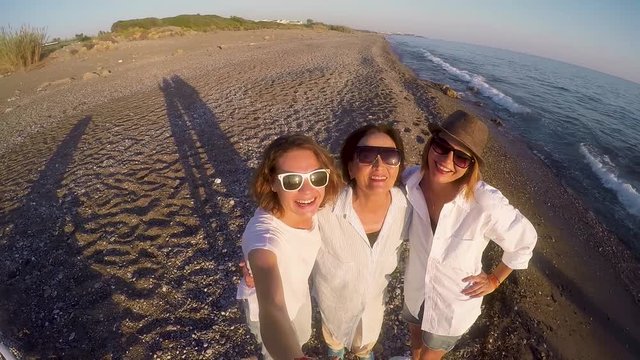 Mother with two adult daughters is taking a selfie on the beach at the sunset time.