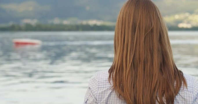 Redhead woman looking at a boat sailing on a lake by summer.
