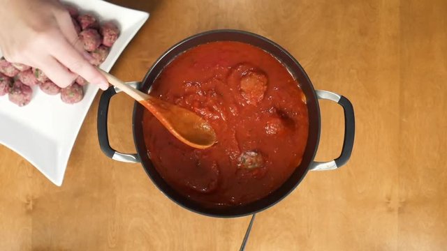 Close up, putting meatballs into pot of marinara