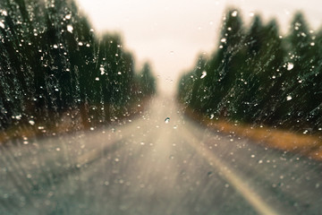 Drops of rain on the window; blurred highway and trees in the background; shallow depth of field