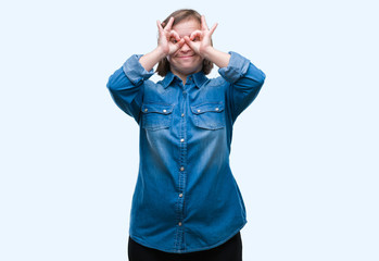 Fototapeta premium Young adult woman with down syndrome over isolated background doing ok gesture like binoculars sticking tongue out, eyes looking through fingers. Crazy expression.