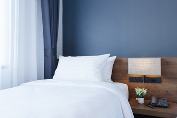Close-up of white pillow on bed decoration with light lamp and digital telephone set in hotel bedroom interior.