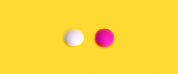 Two pills pink and white on a yellow background. View from above.