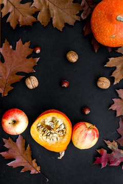 Autumn background. Dried leaves, pumpkin, apple and nuts on black background top view
