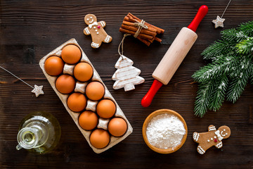 Obraz na płótnie Canvas Cook homemade gingerbread cookies for New Year party. Rolling pin, eggs, flour, cinnamon near gingerbread man and spruce branch on dark wooden background top view