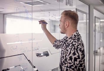one young man, writing on glass window wall of modern office, with marker.