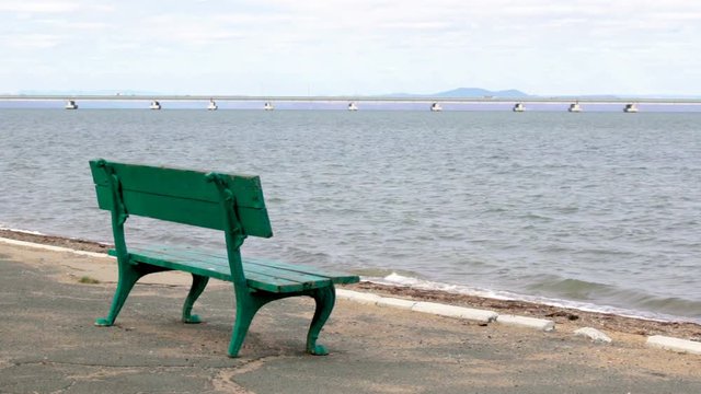 A rest park bench and a view from the shore of a low-water bridge from the Sedanka station to the De Friz peninsula across the Amur Bay in the far east city of Vladivostok.