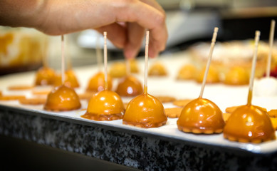 Caramel sweets prepared by a baker on a tray. The baker is placing one of the sweets on the tray. 