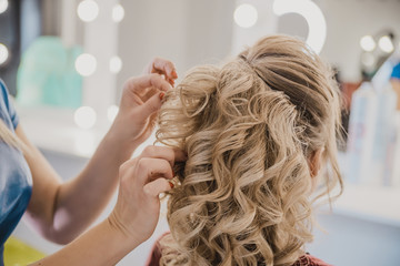Naklejka premium female hairdresser does hair blonde girl in a beauty salon, the process of creating hairstyles