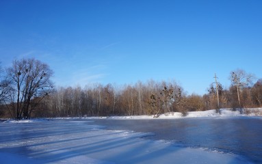 Winter Christmas landscape in pink tones,with calm winter river, surrounded by trees.Winter forest on the river at sunset. Landscape with snowy trees, beautiful frozen river with reflection in water