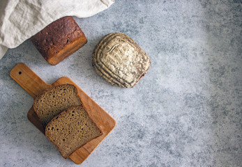 Loaf of bread and pieces of bread on a wooden board on a stone background