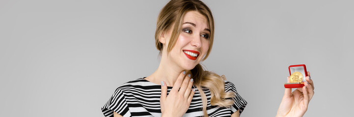 Naklejka premium Attractive young blonde girl in striped blouse smiling showing bitcoin as cryptocurrency concept standing on gray background