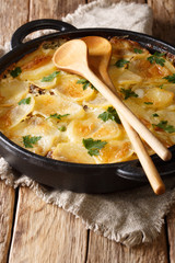Traditional Finnish food Janssonin Kiusaus baked potatoes with anchovies, onions and heavy cream close-up in a frying pan. vertical