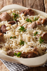 Estonian traditional dish mulgikapsas pork cooked with sauerkraut and barley closeup in a pan. vertical