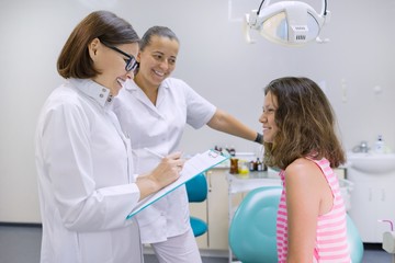 Obraz premium Teenager girl talking with doctors dentists sitting in the dental office. Medicine, dentistry and healthcare concept