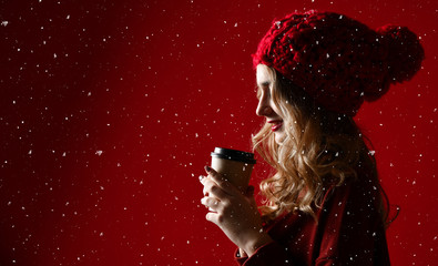 Naklejka premium Pretty brunette woman in warm clothes drinking hot chocolate or coffee on red