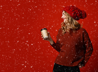 Pretty brunette woman in warm clothes drinking hot chocolate or coffee on red