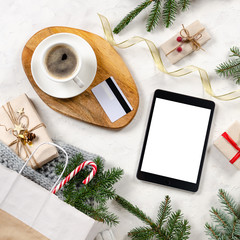 Christmas online shopping. Shopping bag with presents, cup of coffee, tablet and credit card, discount card on white table. top view. Tablet Mock up. Winter holidays sales