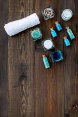 Dead sea cosmetics layout. Sea salt in bottles and bowls near small shells on dark wooden background top view space for text