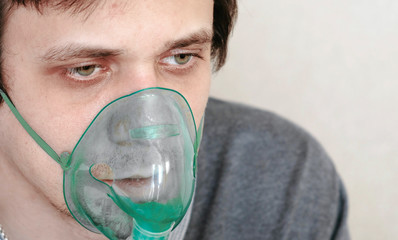 Use nebulizer and inhaler for the treatment. Closeup young man's face inhaling through inhaler...