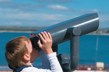 Fototapeta na wymiar Unrecognizable boy looks through binoculars at the sea.