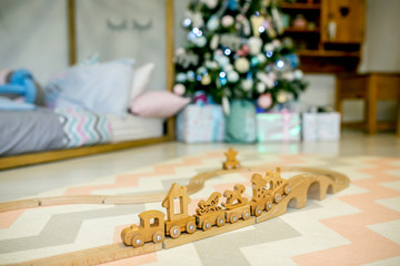 Children bedroom decorated for Christmas. Wooden toy railway on the background of the Christmas tree lights and bed. Christmas morning. Holiday mood