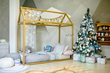 Children bedroom decorated for Christmas. Big wooden frame bed with pillows and plush toys, Christmas tree with balls, ribbons and gifts under it. Christmas morning. Holiday mood