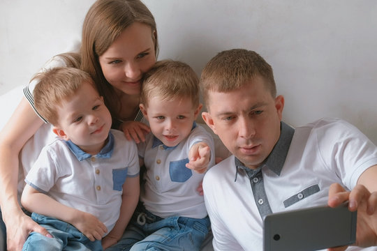 Dad makes family selfie on mobile phone. Mom, dad and two brother twins toddlers.