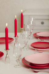 Merry Christmas and Happy New Year! Table setting - red and pink dishes, holiday knitted decor - Santa Claus knitted hats on the bottle with wine, red candles.