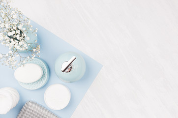 Fashion cosmetic products set on pastel blue color paper - white soap, towel, flowers, soap dispenser, blue ceramic vase, silver cosmetic bag, top view, copy space.