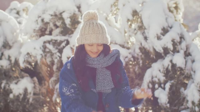 Winter girl throwing snowball at camera smiling happy having fun outdoors on snowing winter day playing in snow. Cute playful multicultural Asian Caucasian young woman outdoor enjoying first snow