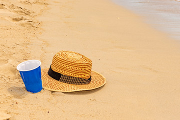 Plastic cup and hat on the beach sands as vacation concept.