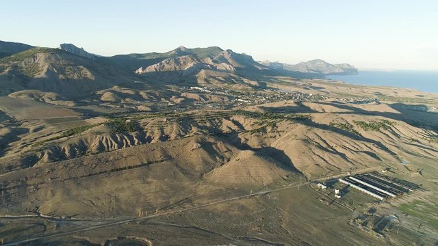Top view of desert mountain ranges and town. Shot. Panorama of meager green hills and mountain horizon with sea shore