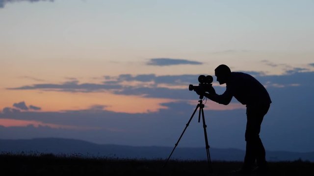 Man silhouettes with photo camera on tripod take pictures at sunset sky