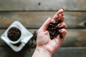 Coffee beans in the female palm, and on a blurred background a cup with coffee beans on a wooden table